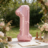 A pink foil number balloon shaped like the number one with bows, displayed outdoors on a white table.