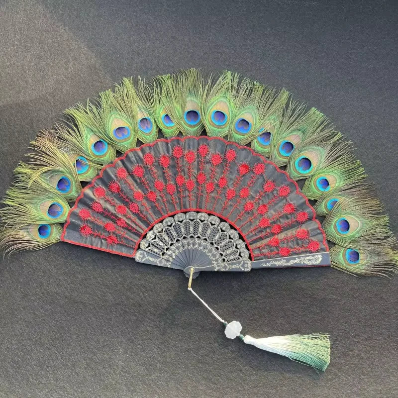 Un éventail à main en plume de paon naturel avec des plumes vertes et bleues vibrantes et une surface d'éventail rouge et noi
