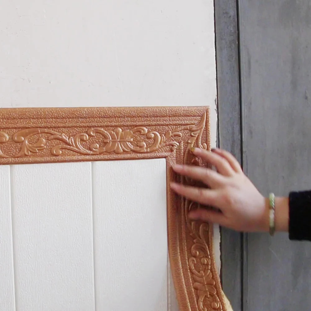 A hand is touching a brown 3D self-adhesive wall trim border featuring an ornate scroll design on a white panel.