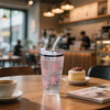 A clear plastic cup with pink bow decorations, straw, and lid sits on a wooden table.