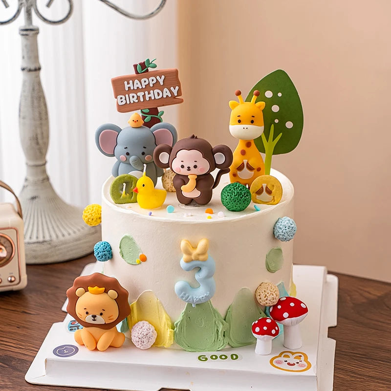 A tiered cake decorated with jungle safari animal toppers including a giraffe, elephant, monkey, and lion.