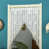 White embroidered sheer lace door curtain with tassels hanging in a white frame against a teal wall.