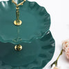 A two-tier serving stand in deep teal ceramic with gold accents, featuring scalloped edges.