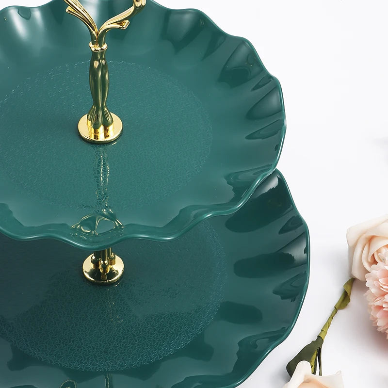 A two-tier serving stand in deep teal ceramic with gold accents, featuring scalloped edges.