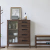 A wooden cabinet with drawers and a glass door, featuring dark handles and a framed sketch on the wall.