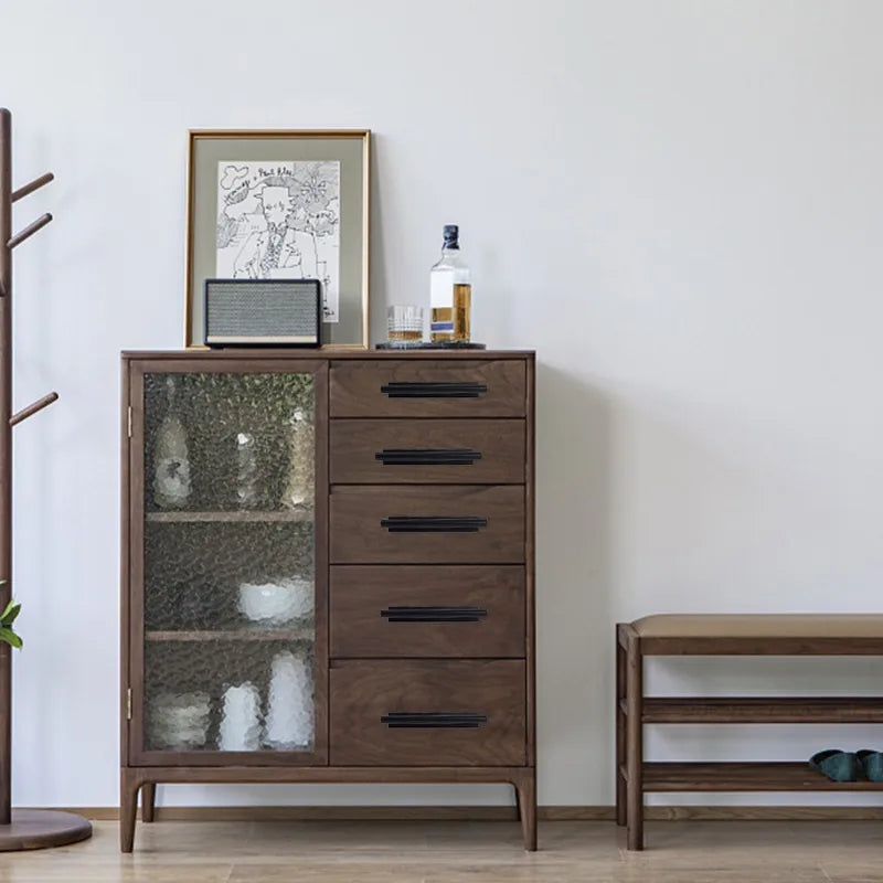 A wooden cabinet with drawers and a glass door, featuring dark handles and a framed sketch on the wall.
