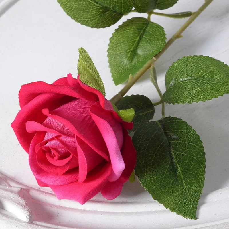 A vibrant pink velvet artificial rose with green leaves on a white background.