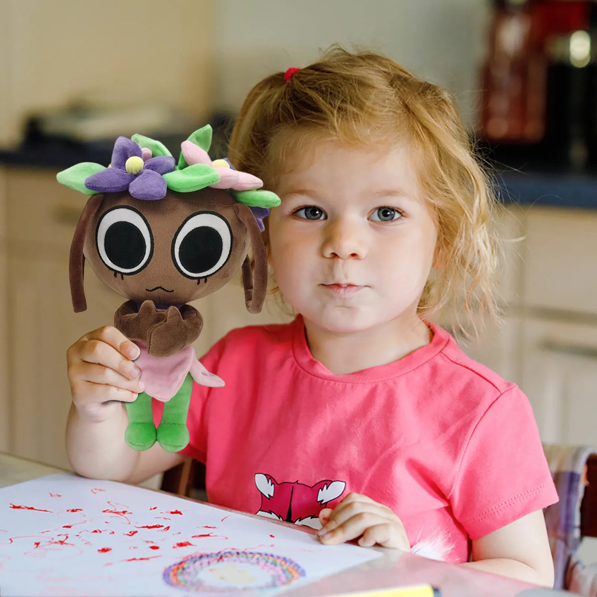 A young girl holds a brown plush toy with purple flowers and green accents in front of her.