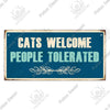 A rustic wooden sign with blue lettering that reads Cats Welcome People Tolerated and features a leafy border.