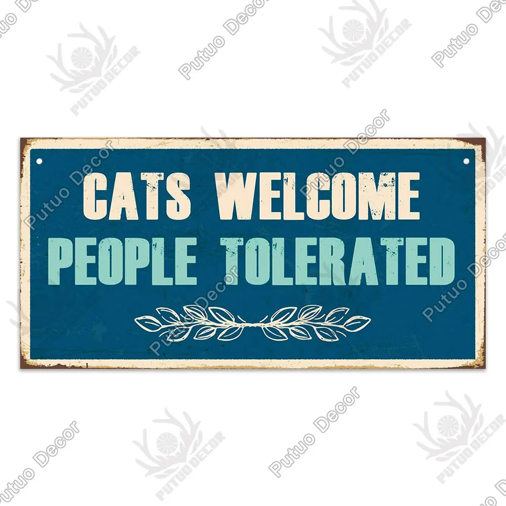 A rustic wooden sign with blue lettering that reads Cats Welcome People Tolerated and features a leafy border.