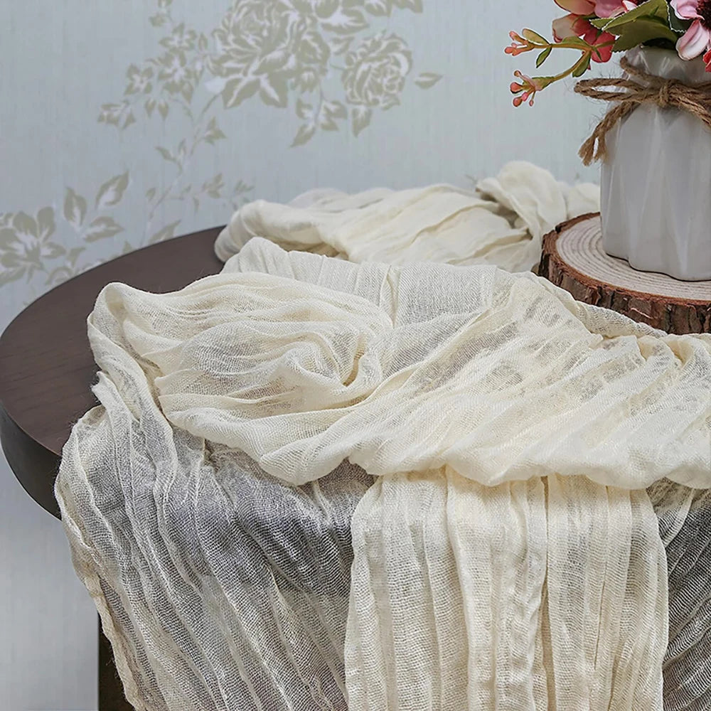 A sheer beige gauze table runner draped over a dark wooden table with a floral wallpaper background.