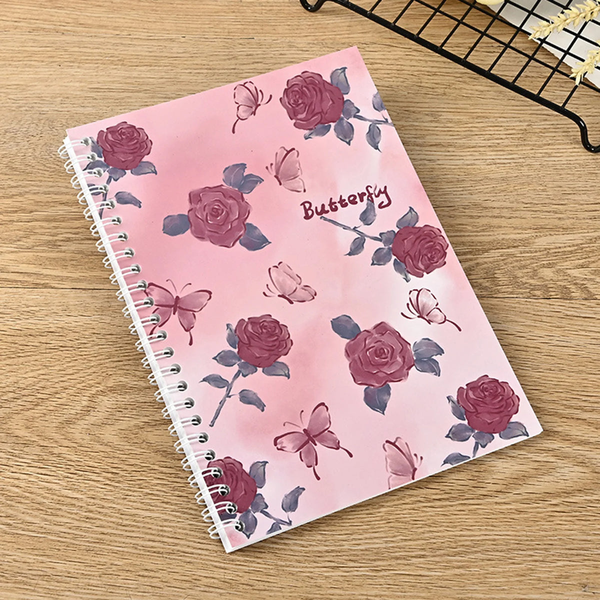 A pink spiral notebook featuring a floral pattern of roses and butterflies for sticker collecting.