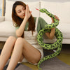 A woman is holding a large, realistic green snake plush toy with patterned skin, sitting on a light sofa.