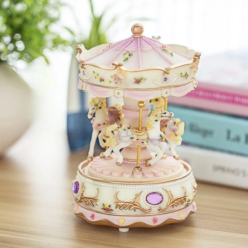 A delicate pink and gold resin carousel music box with horses and floral accents.
