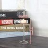 Elegant tall glass candle holder with a lit candle placed among stacked books.