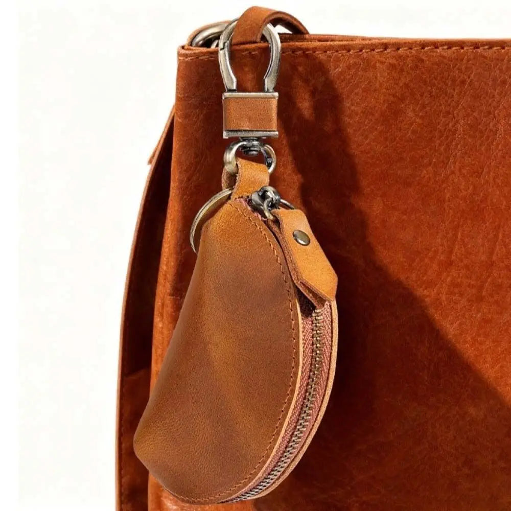 A brown leather key pouch with a metal carabiner attached, shown against an orange-brown leather bag.