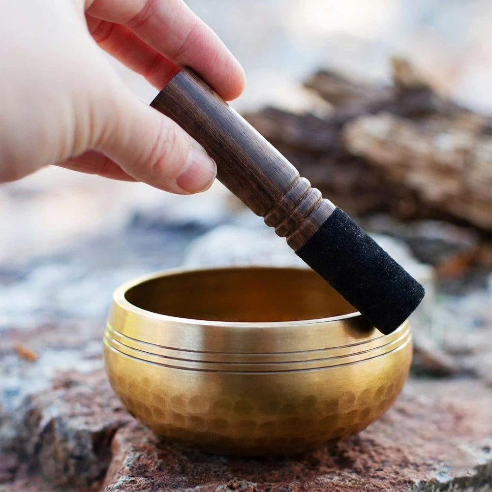 A hand holds a handcrafted copper singing bowl resting on a rough stone surface.