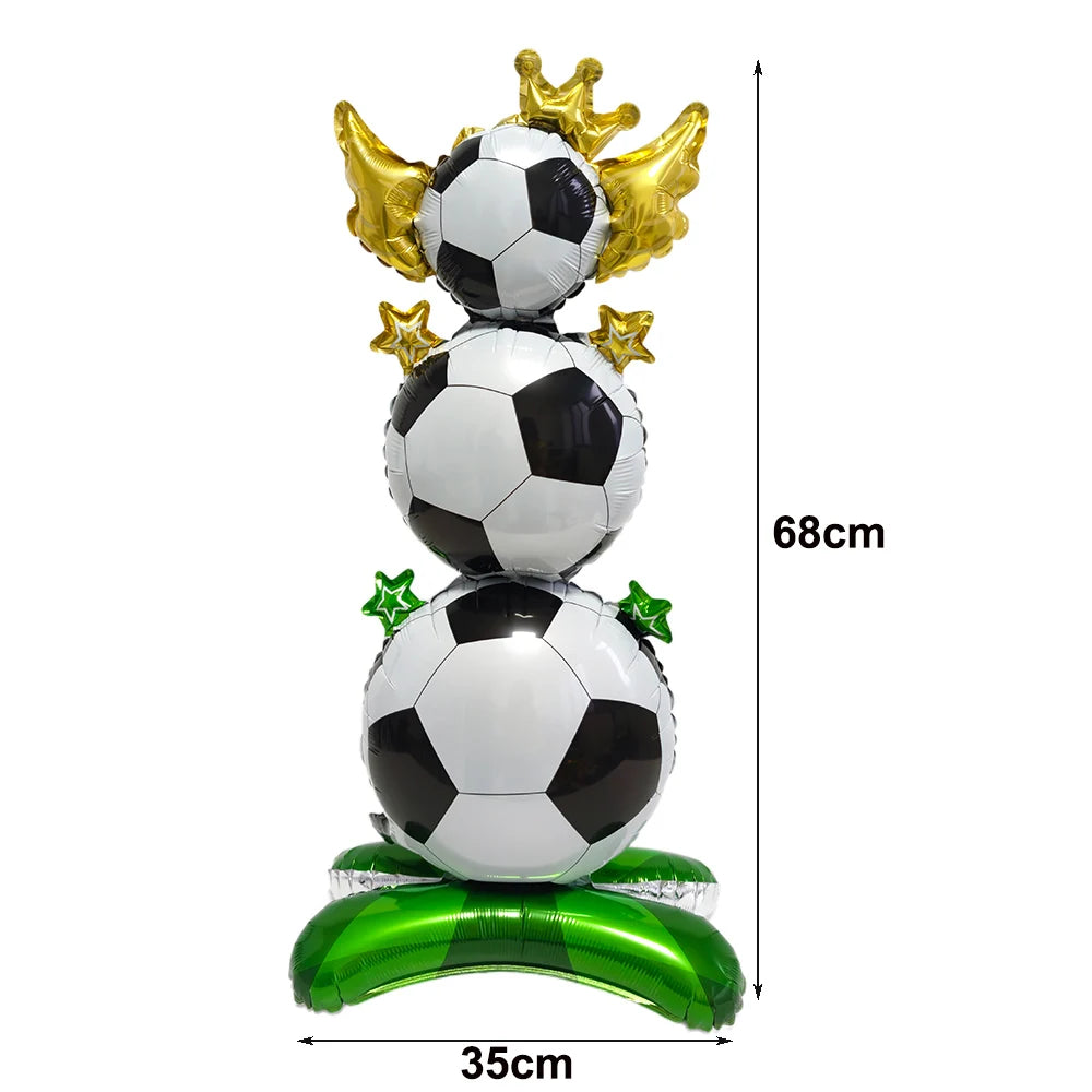 A standing soccer balloon decoration featuring three stacked footballs in black and white with gold accents on a green base.
