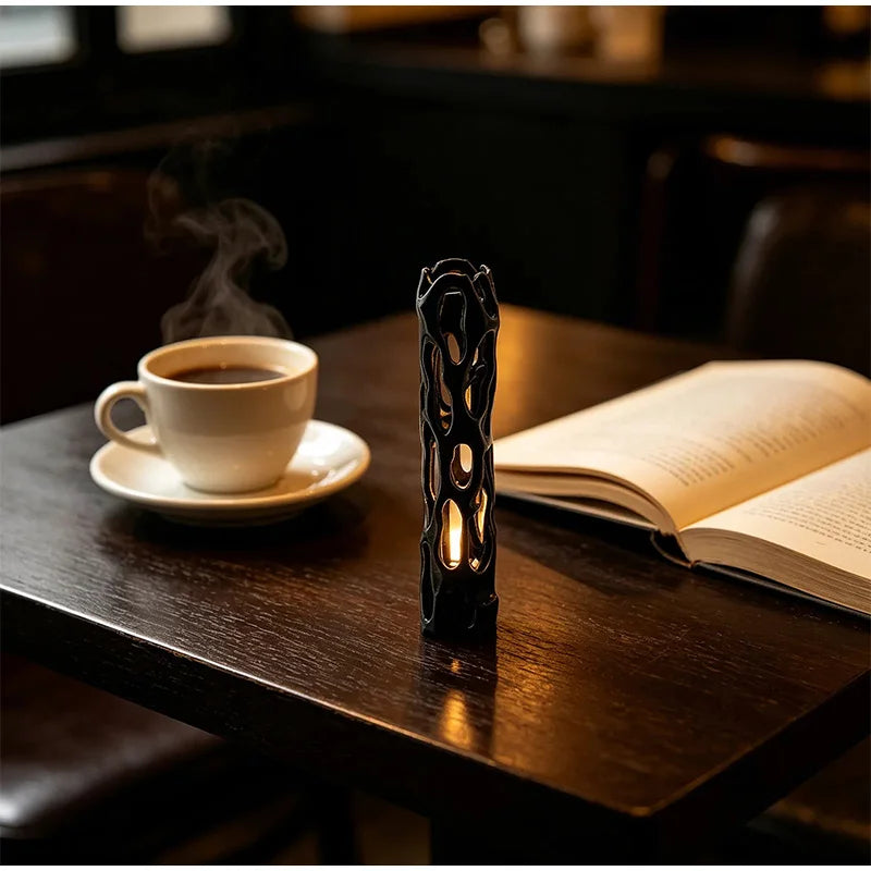 A dark wooden table features a cup of coffee, an open book, and a black 3D printed wishing willow stick candle.