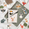 A collection of assorted animal stickers featuring deer, owls, penguins, and other wildlife designs on a gray notebook.