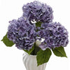 A bouquet of large purple hydrangea flowers with green leaves in a white vase.