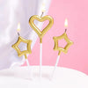 A set of two gold heart and star birthday candles on a white surface.