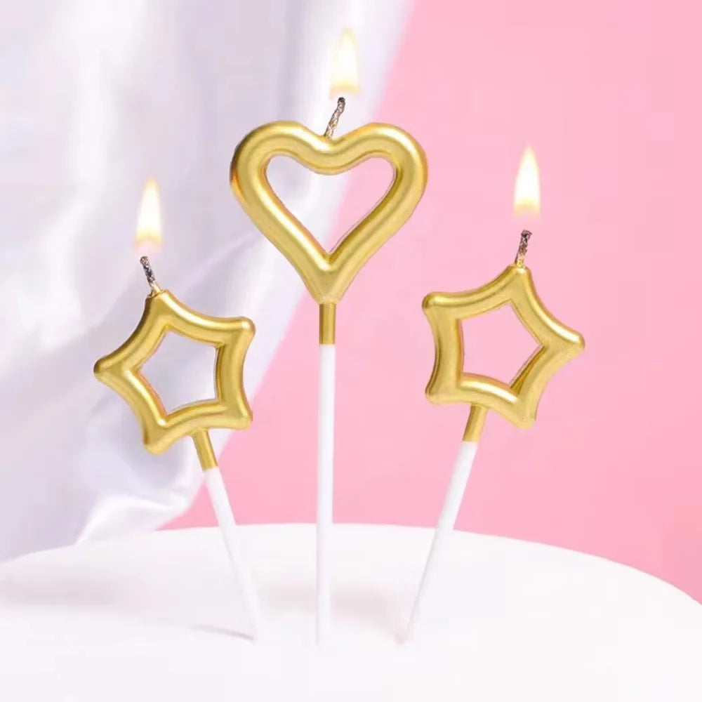 A set of two gold heart and star birthday candles on a white surface.