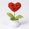 Hand woven crochet heart flower in red atop a green plant in a white pot