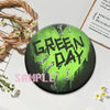 A set of green button pins with the text GREEN DAY printed in a distressed style on a dark background.