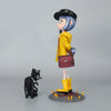 A figurine of a blue-haired girl in a yellow coat and black hat standing next to a small black cat.