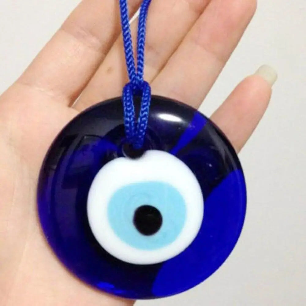 A dark blue glass evil eye amulet pendant with a white iris and blue surrounding glass is held in a hand.