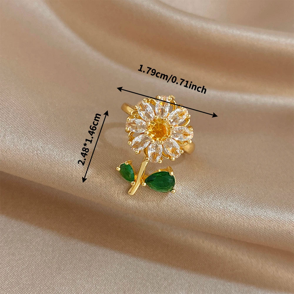A close-up of an elegant cocktail ring featuring a gold setting and a flower design with green leaves.