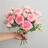A hand holds a bouquet of pink silk peony roses for weddings and home decor.