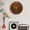 Minimalistische, runde Holz-Wanduhr in Roségold auf weißer Wand neben einer Marshall-Gitarrentasche.