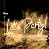 A glowing neon sign spelling out Let's Party in cursive script, set against a dark background with dry grass.