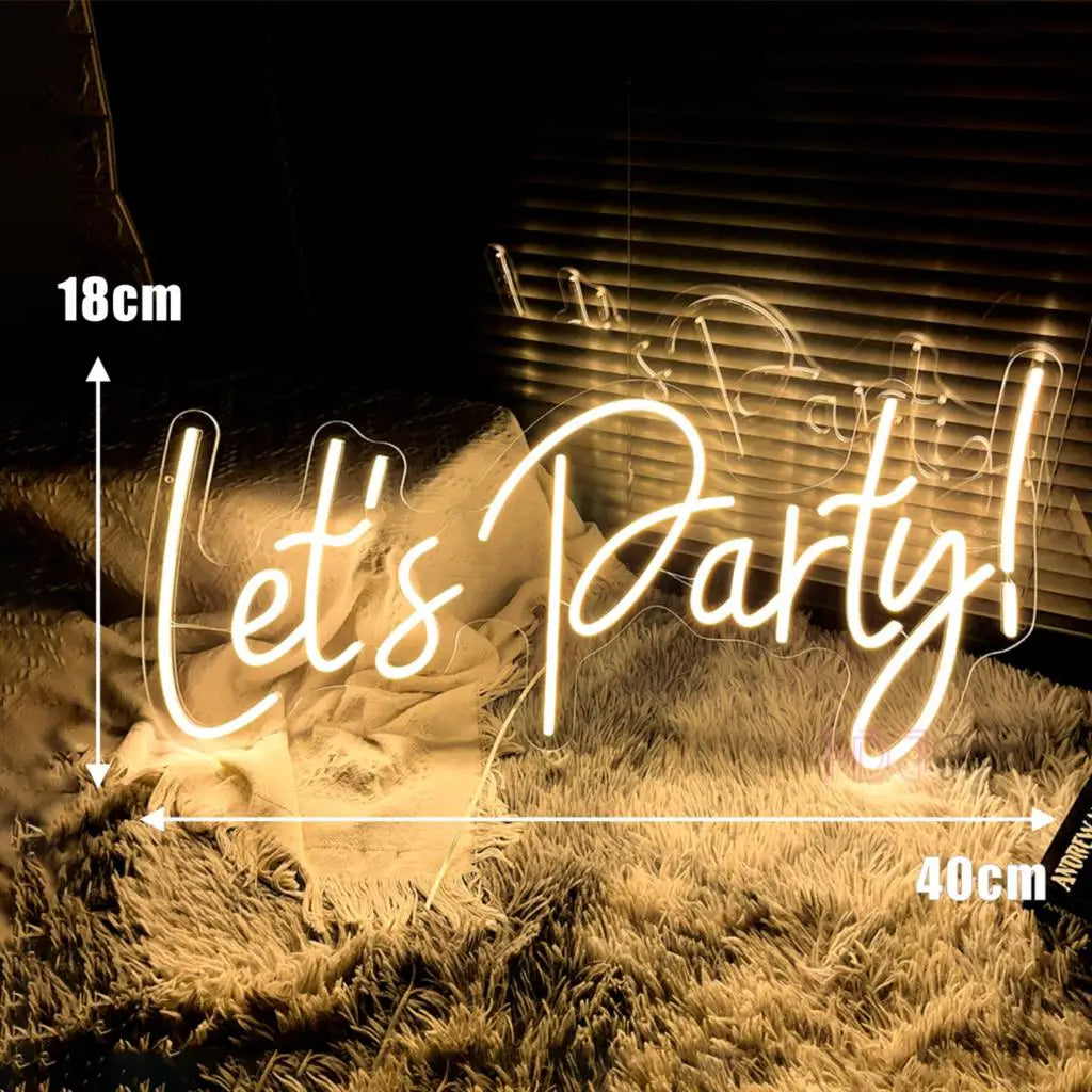 A glowing neon sign spelling out Let's Party in cursive script, set against a dark background with dry grass.