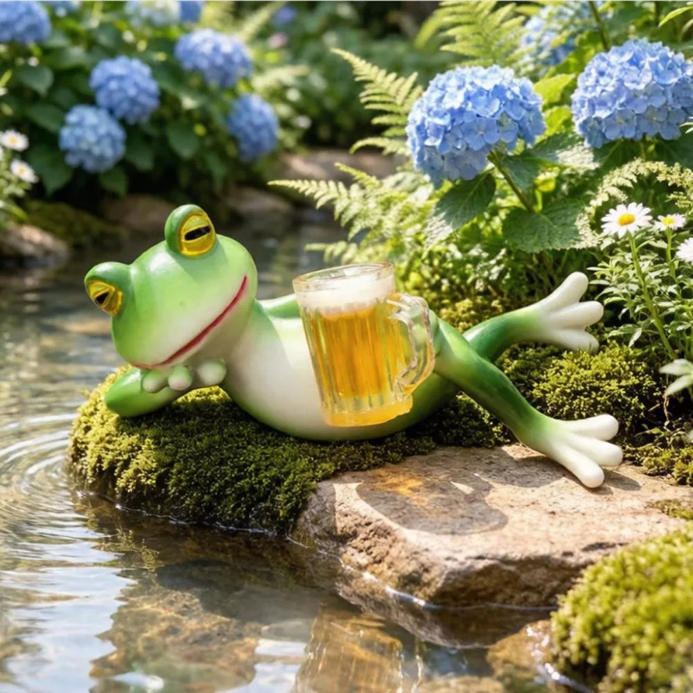 Figura de rana de resina verde descansando en una roca musgosa cerca del agua y la vegetación.