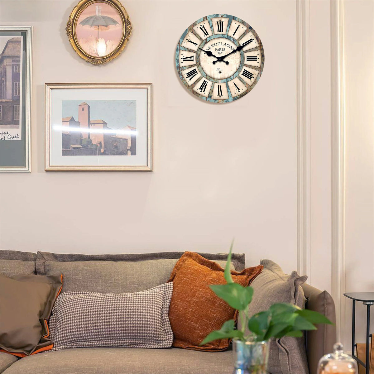 A rustic wooden wall clock with a blue and white face hangs on a light-colored wall above a sofa.