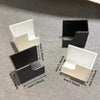 A set of black and white space-saving scale storage holders with self-adhesive mounts displayed on a gray surface.
