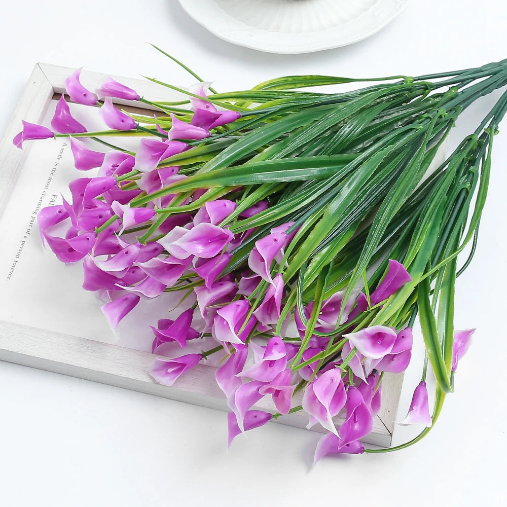 A bouquet of purple artificial calla lily flowers with green stems displayed on a light wooden tray.