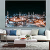 A canvas wall art print depicting the Kaaba and Al Masjid An Nabawi at night, displayed in a living room setting.