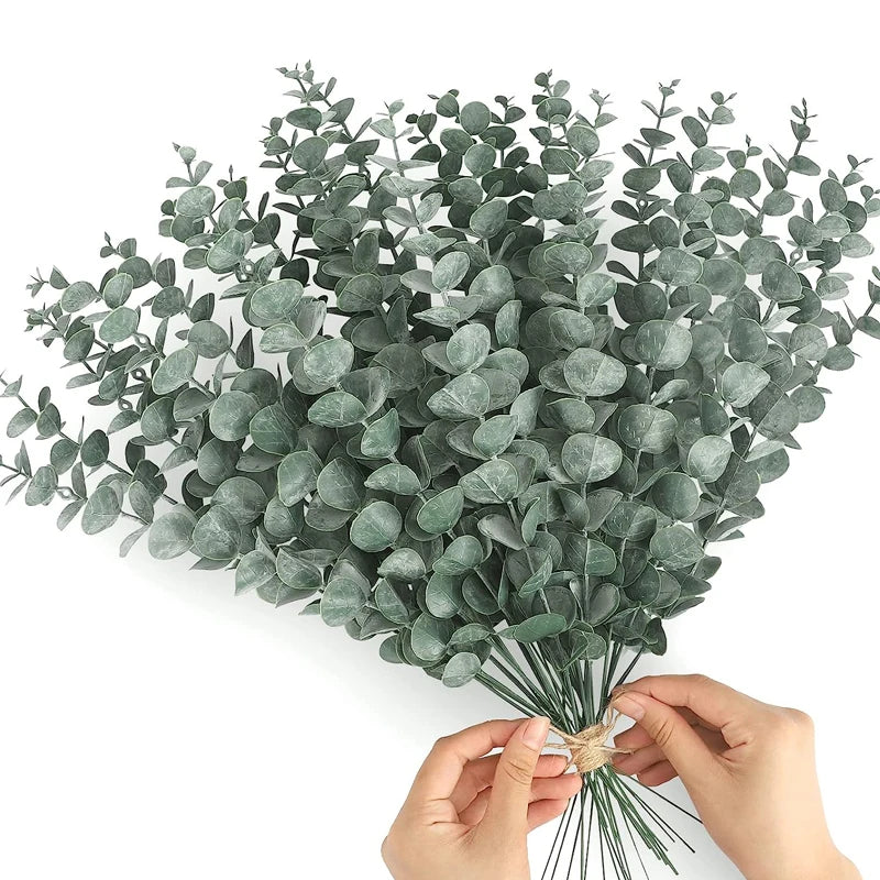 A bunch of artificial eucalyptus stems with silvery-green leaves held by a person's hands.
