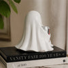 Décor fantôme en résine blanche drapé d'un voile reposant sur un livre intitulé Vanity Fair 100 Years