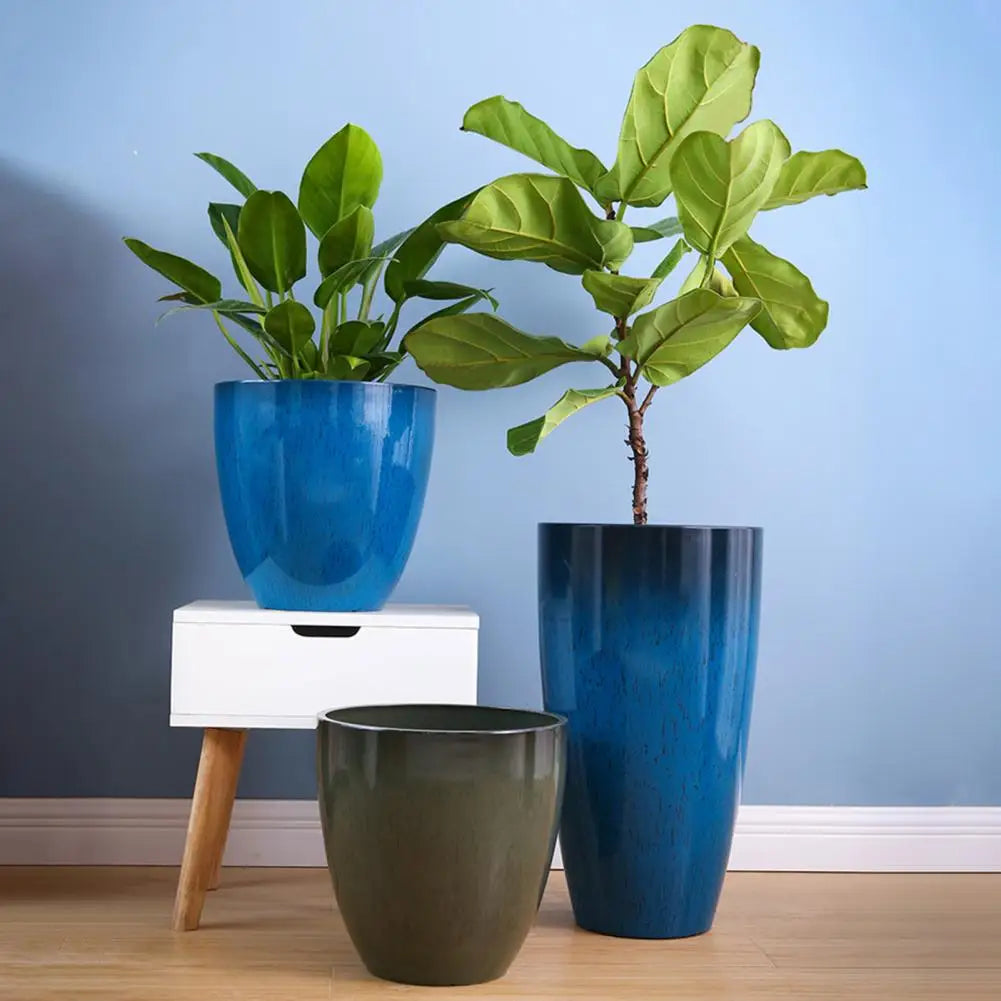 A large blue resin monstera plant in a tall blue ceramic planter sitting on a white wooden stand.