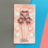 A pink cardboard packaging for a set of metallic heart and star birthday candles against a blue background.