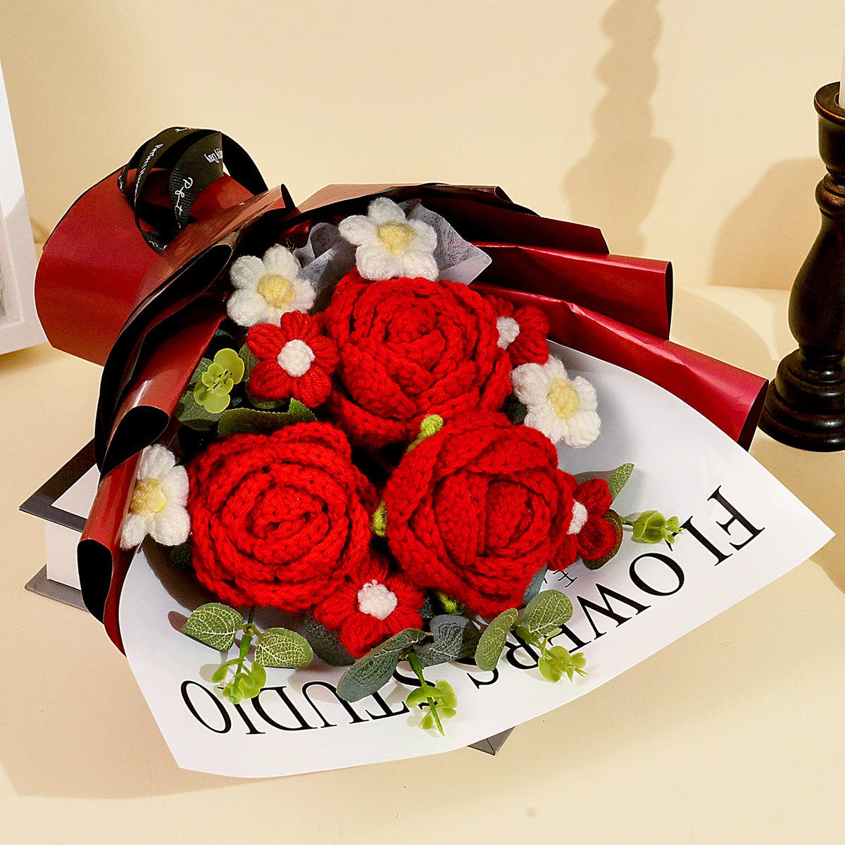 A bouquet of handcrafted red crochet roses wrapped in dark red paper and presented on a white card.