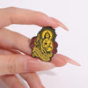 A hand holds a gold enamel pin featuring the image of Saint Jude Thaddeus with the inscription San Judas Tadeo