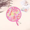 A pink portable foldable cooling handheld fan with a floral pattern is shown next to some paper and a branch of dried flowers