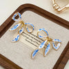 Gold and blue and white porcelain bow stud earrings displayed on a wooden tray