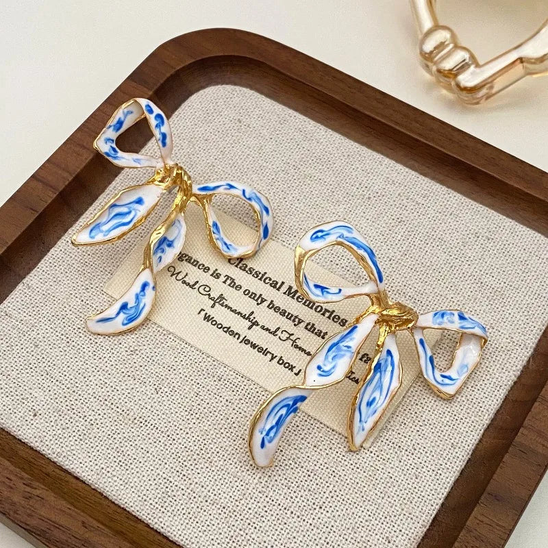 Gold and blue and white porcelain bow stud earrings displayed on a wooden tray